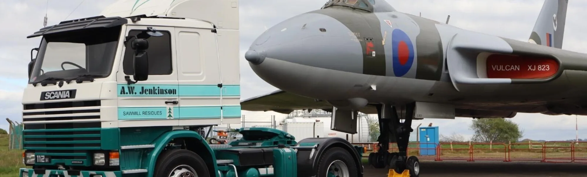 A.W. Jenkinson C-reg Scania parked next to military aircraft at Carlisle Lake District Airport.